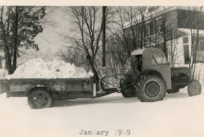 January 1949 – Armed with a new camera, ML Shaw took this image of a Ford Ferguson tractor, sporting a new cab which they built in the basement of Winthrop’s home on Hildreth Street. It’s pulling a load of snow on a hydraulic trailer that Warren (Sr.) and Winthrop built.